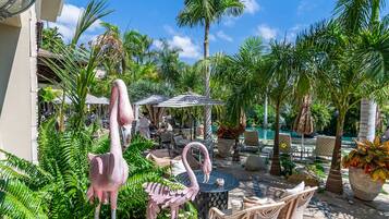 A tropical outdoor area with flamingo statues, wicker furniture, and a pool.