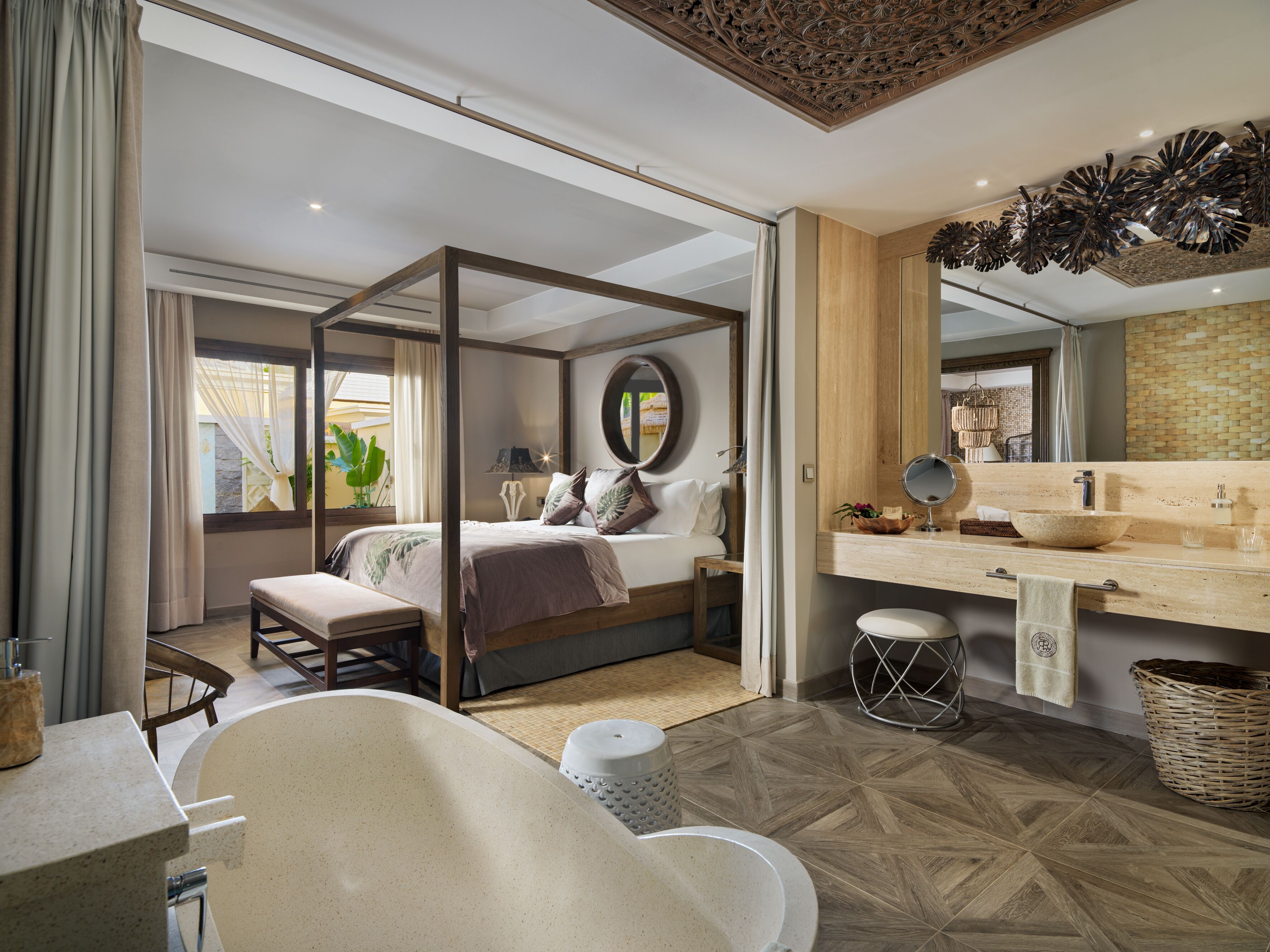 A modern bedroom with a canopy bed, a large mirror, a wooden ceiling, and a bathroom with a bathtub and sink.