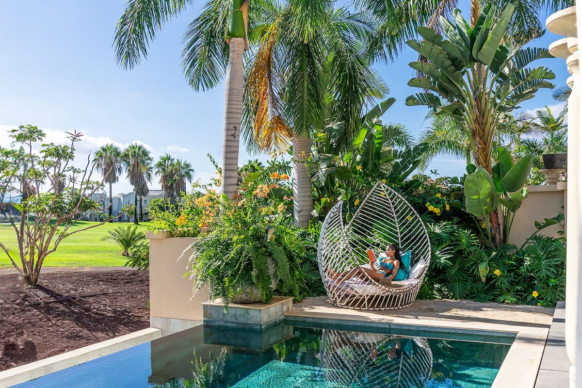 A pool area with a hanging chair, lush tropical plants, and a clear view of the surrounding landscape.