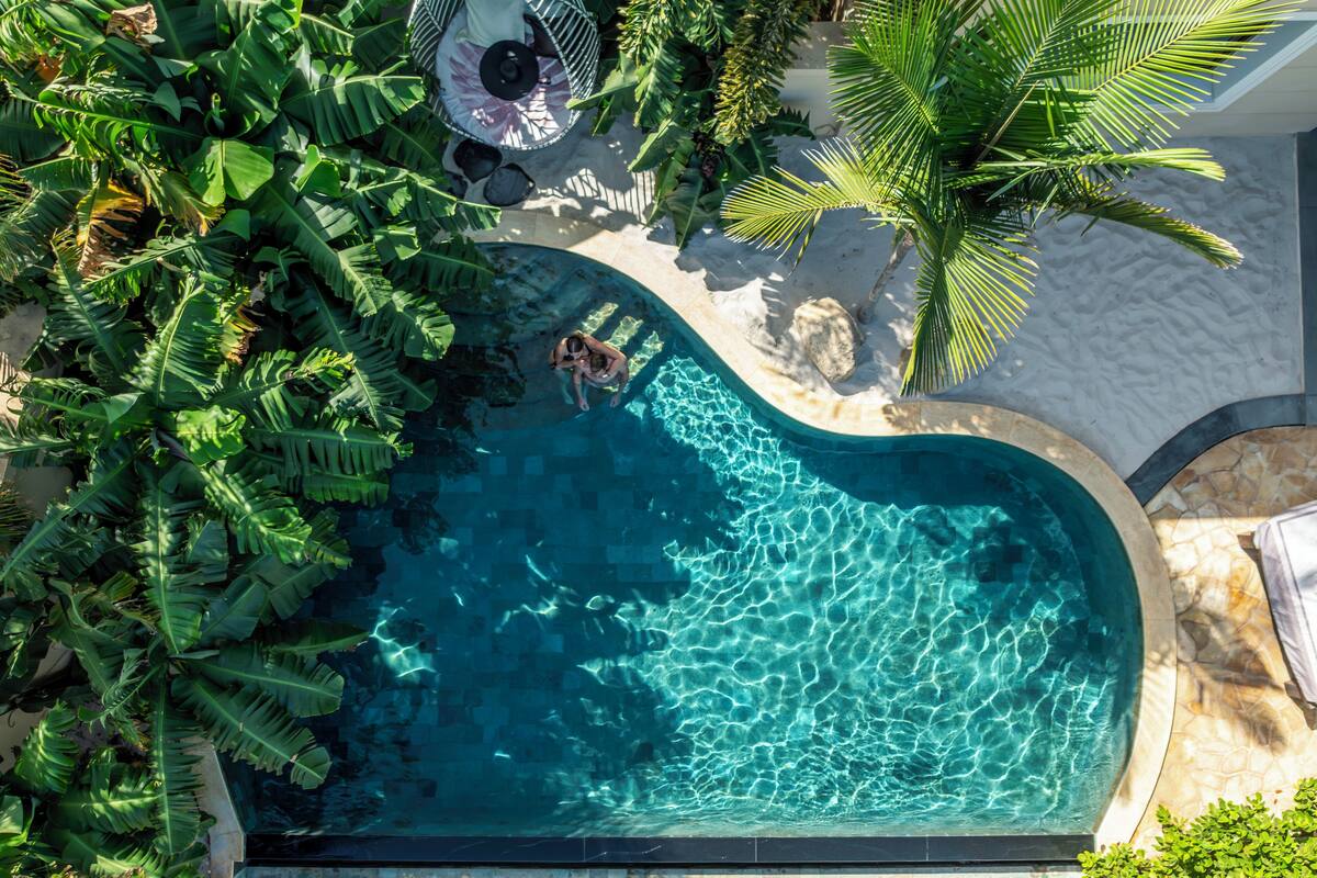 An aerial view of a swimming pool surrounded by lush greenery and a sandy area.