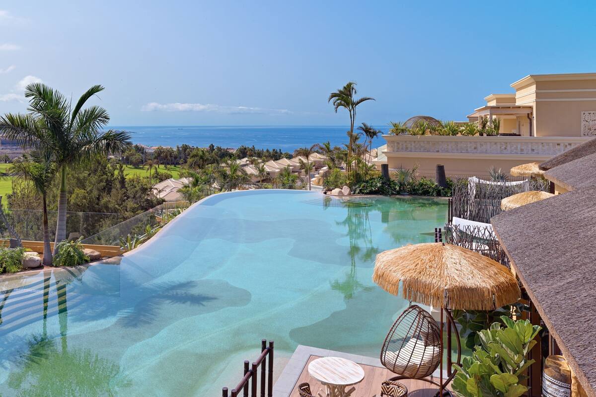 A resort pool with clear water, surrounded by palm trees and a view of the ocean.