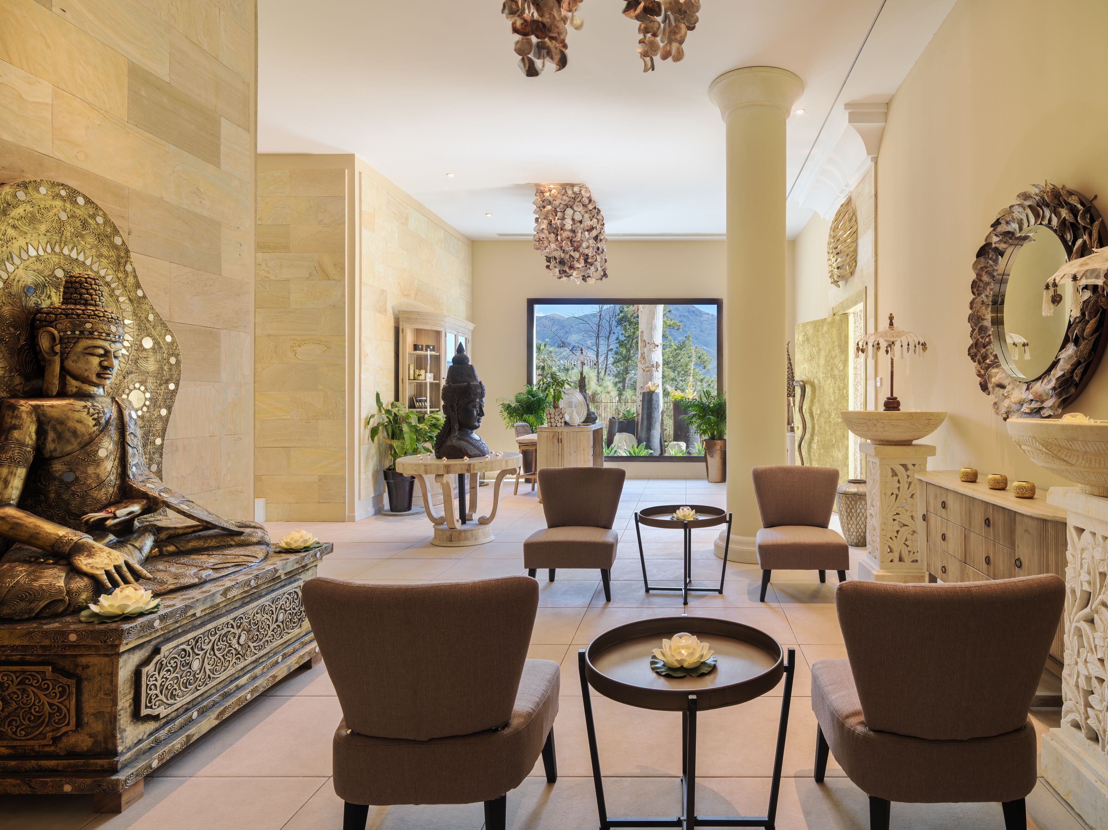 A spacious lobby with a Buddha statue, comfortable seating, a large window with a mountain view, and a decorative mirror.