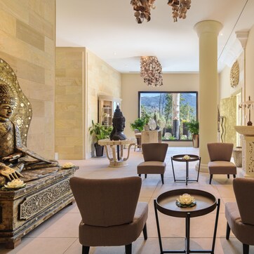 A spacious lobby with a Buddha statue, comfortable seating, a large window with a mountain view, and a decorative mirror.