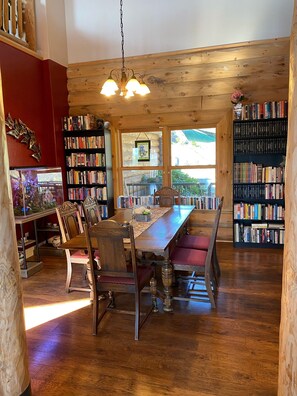 A cozy library with wooden bookshelves, a long dining table with chairs, and a chandelier.