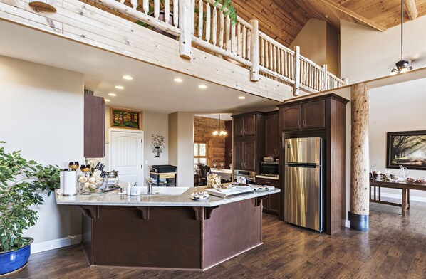 A spacious kitchen with a large island, dark wooden cabinets, stainless steel appliances, and a wooden balcony.