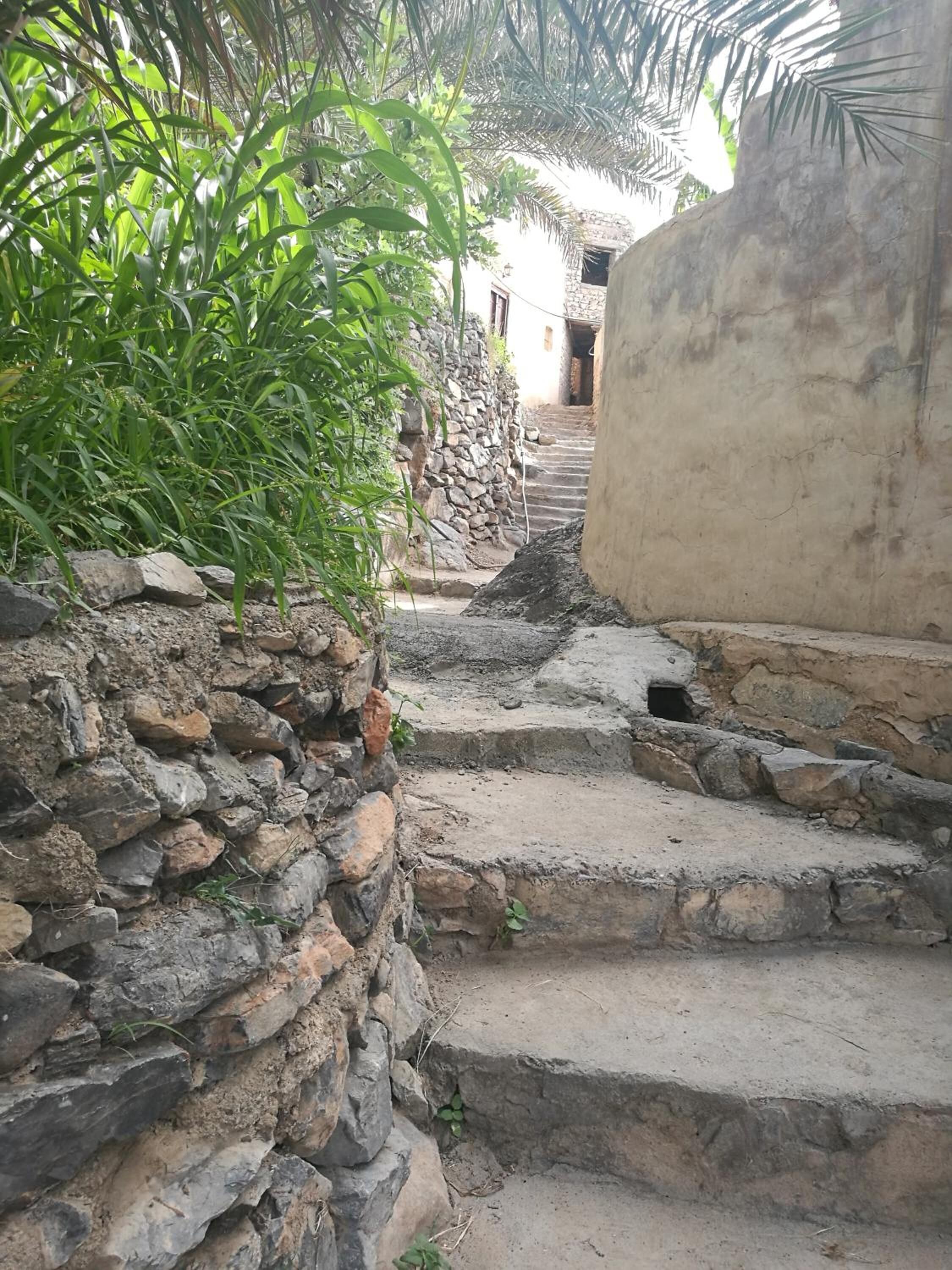 Un escalier étroit en pierre mène à un bâtiment dont un côté est constitué d’un mur de pierre et l’autre d’un mur en béton.
