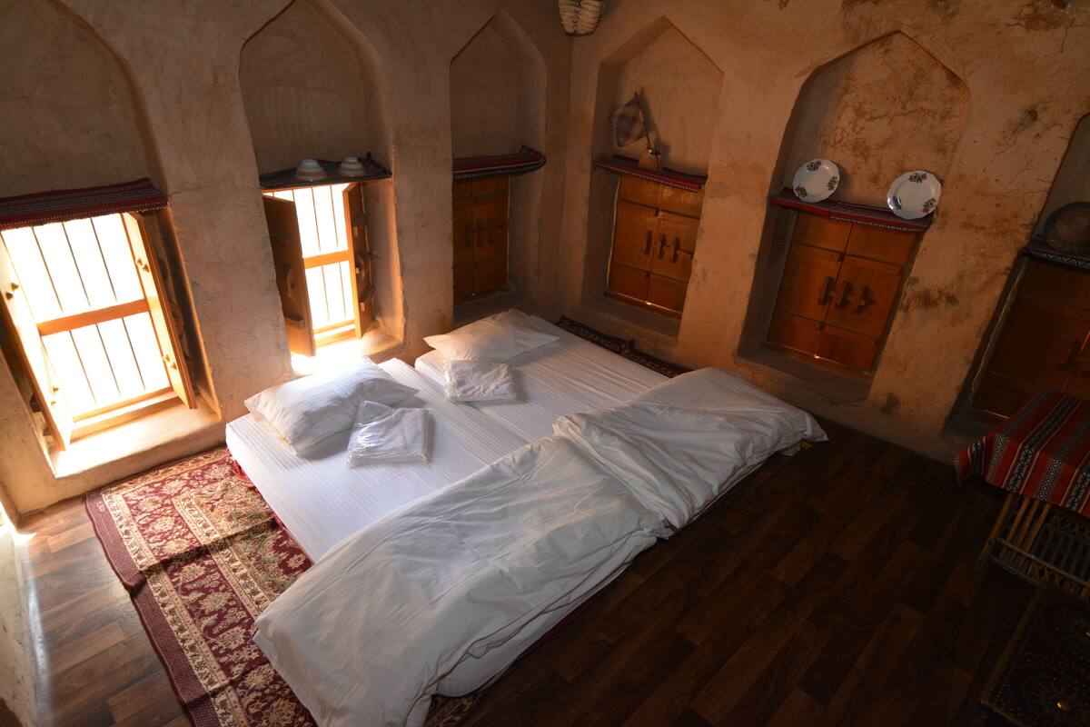 A room with a large bed, wooden floor, arched windows, and traditional decor.