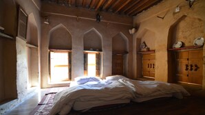 A bedroom with a large bed, wooden beams, and arched windows. - Misfah Old House (Al Hamra)