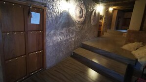 A room with a textured stone wall, wooden steps, and a wooden door with a sign. - Misfah Old House (Al Hamra)