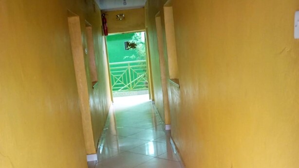 A corridor with yellow walls and white tiled flooring, leading to a green gate. - Elpaso Lodge (Karatina)