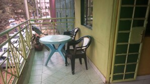 A balcony with a table and chairs, a potted plant, and a view of the street. - Elpaso Lodge (Karatina)
