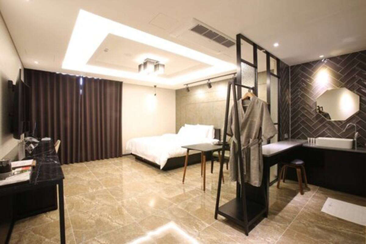Habitación de hotel moderna con cama, escritorio, silla y baño con lavamanos y espejo.