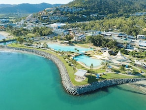 Vue aérienne d’une station balnéaire dotée de plusieurs piscines, d’une côte rocheuse et d’immeubles résidentiels.