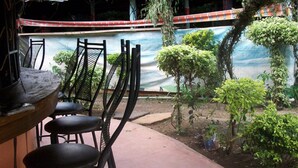 A patio area with metal chairs and a table, surrounded by greenery and a mural on the wall. - Mark5 Resort (Njumbi)