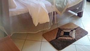A room with a bed covered by a mosquito net, a small table with a chair, and a window with curtains. - Mark5 Resort (Njumbi)