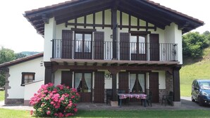 Un edificio de dos pisos con un balcón, pilares de piedra y una pequeña mesa con sillas afuera.