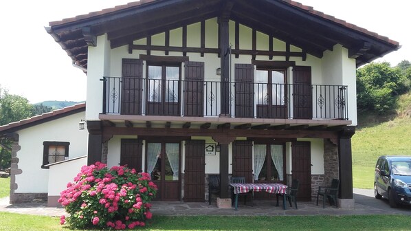 A two-story building with a balcony, stone pillars, and a small table with chairs outside.