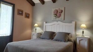 Un dormitorio con una cama, dos mesitas de noche con lámparas, un ventanal con cortinas y una obra de arte en la pared.