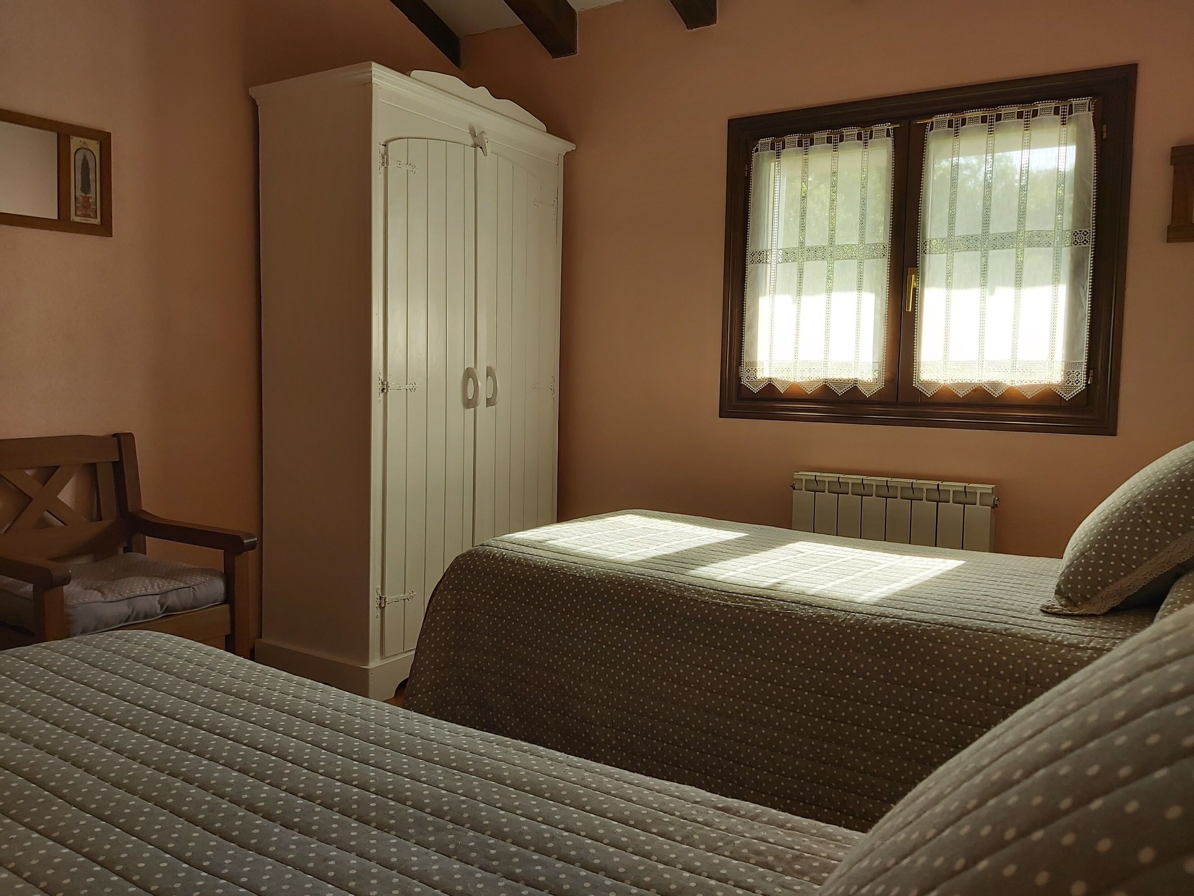 Een slaapkamer met een bed, een kledingkast, een stoel en een raam met kantgordijnen.