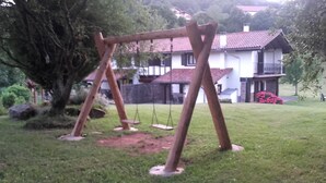 Un columpio de madera en un patio cubierto de césped, con una casa al fondo.