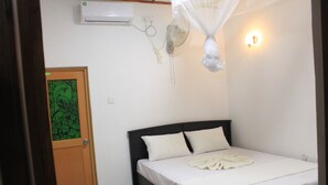 A bedroom with a bed, a bedside table, an air conditioner, a wall-mounted fan, and a door with a green patterned glass panel.