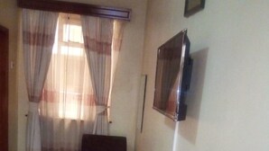 A room with a wooden table, a television mounted on the wall, and a window with curtains.