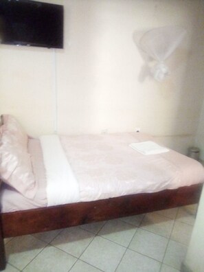 A single bed with a wooden frame, a white mattress, and a pink bedspread.