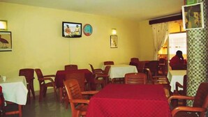 A dining area with wooden tables and chairs, a clock, and framed pictures on the walls.