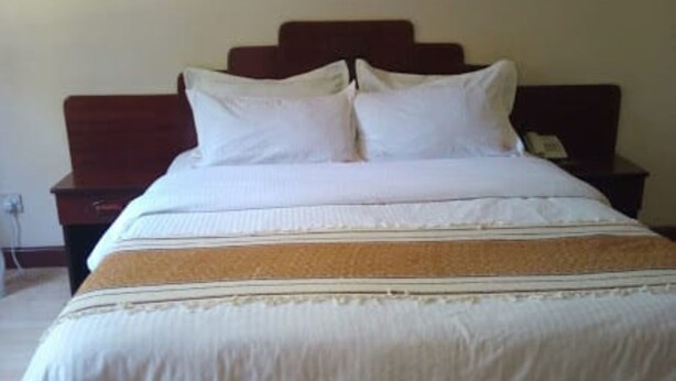 A neatly made bed with white bedding and a brown headboard, a wooden nightstand with a phone, and a wall socket.