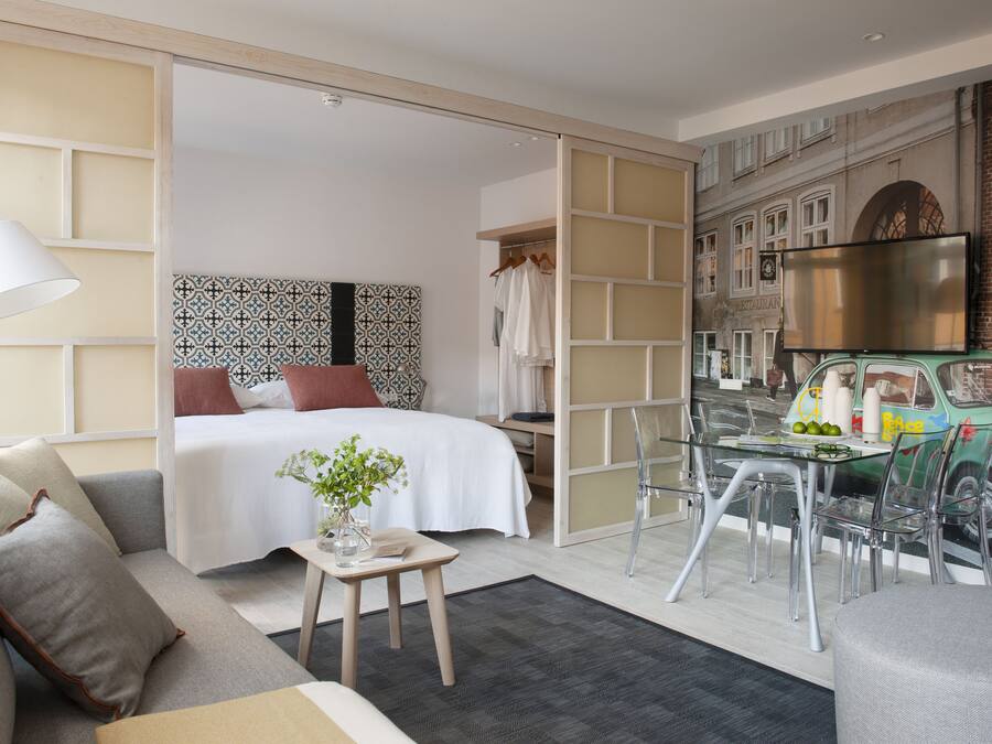 Una habitación de hotel moderna con cama, sofá, una mesita y televisor.