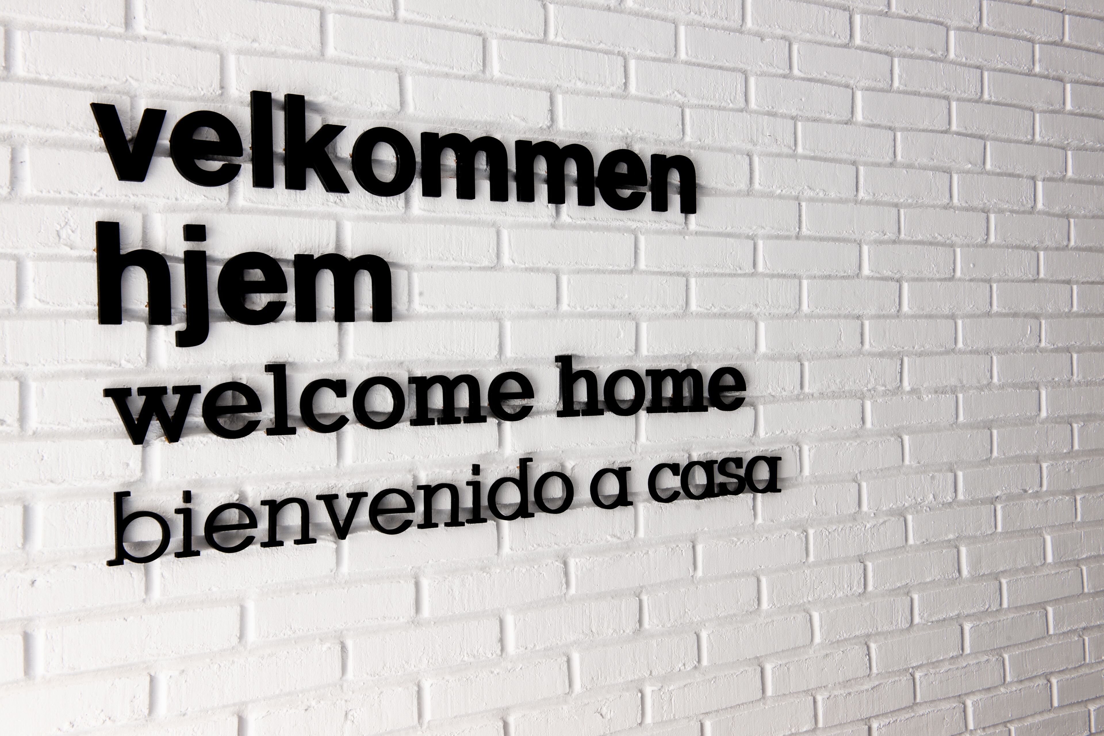 Un mur en briques blanches sur lequel figure un texte dans trois langues : « velkommen », « hjem » et « welcome home ».