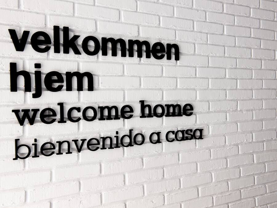 Un muro de ladrillo blanco con texto en tres idiomas: 'velkommen', 'hjem' y 'welcome home'.