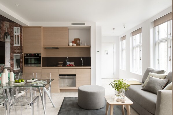 A modern kitchen with a dining area, a grey ottoman, and a sofa with cushions. - Eric Vökel Boutique Apartments - Copenhagen Suites (Copenhagen)