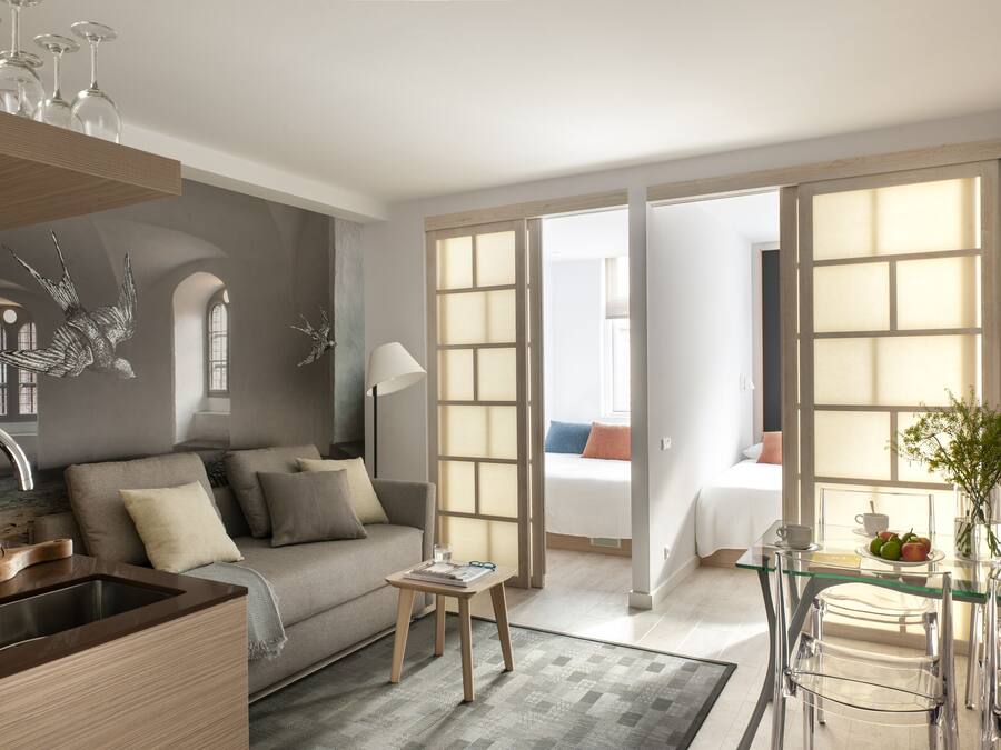 Quarto de hotel moderno com cozinha compacta, sofá, área de refeições e uma grande janela com vista.