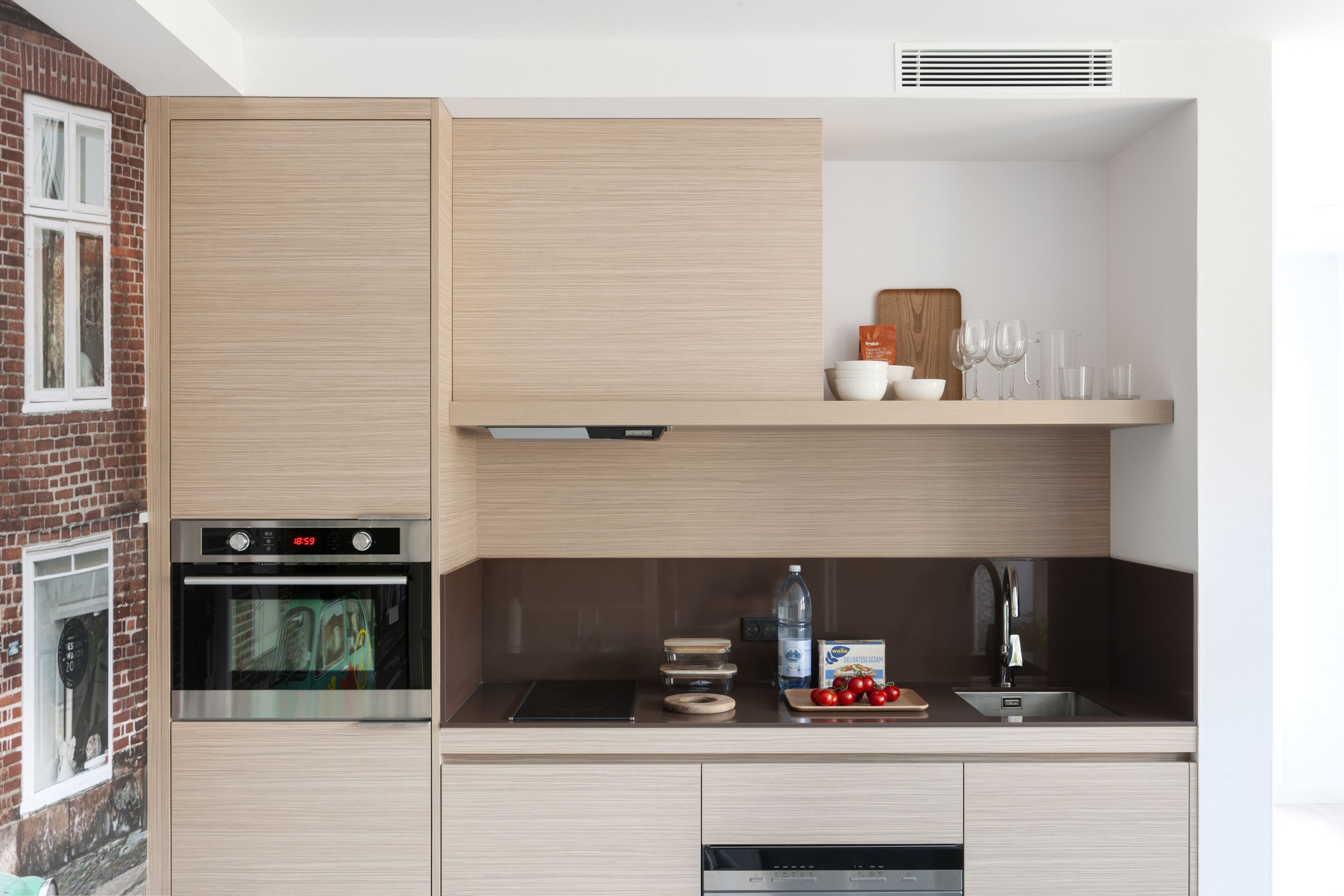 A modern kitchen with a built-in oven, a microwave, and a sink. There are wooden cabinets and a countertop with various kitchen items.