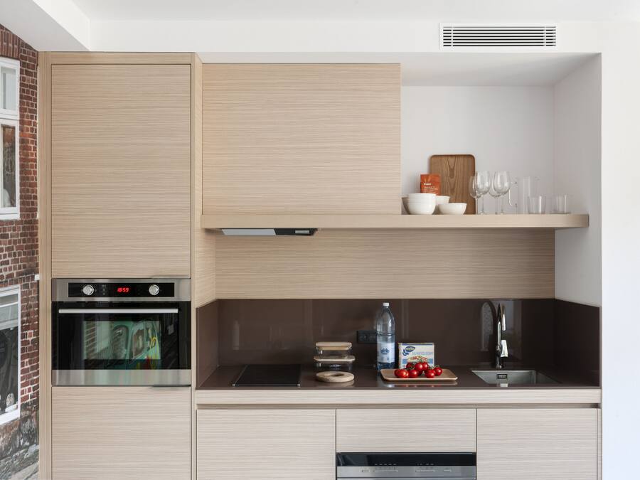 A modern kitchen with a built-in oven, a microwave, and a sink. There are wooden cabinets and a countertop with various kitchen items.