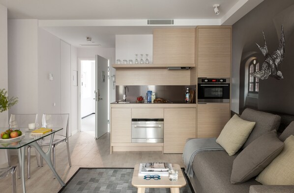 Una cocina moderna con electrodomésticos integrados, una zona de comedor con una mesa de vidrio y un salón con sofá.