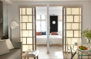 A modern hotel room with a sofa, a small table with a book and glasses, a glass table with a bowl and fruit, and a bed with pillows. - Eric Vökel Boutique Apartments - Copenhagen Suites (Copenhagen)