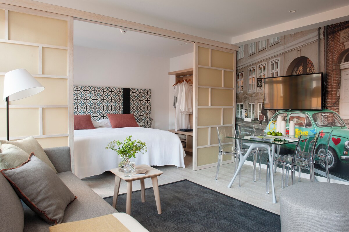 Una habitación de hotel moderna con cama, sofá, una mesita y televisor.