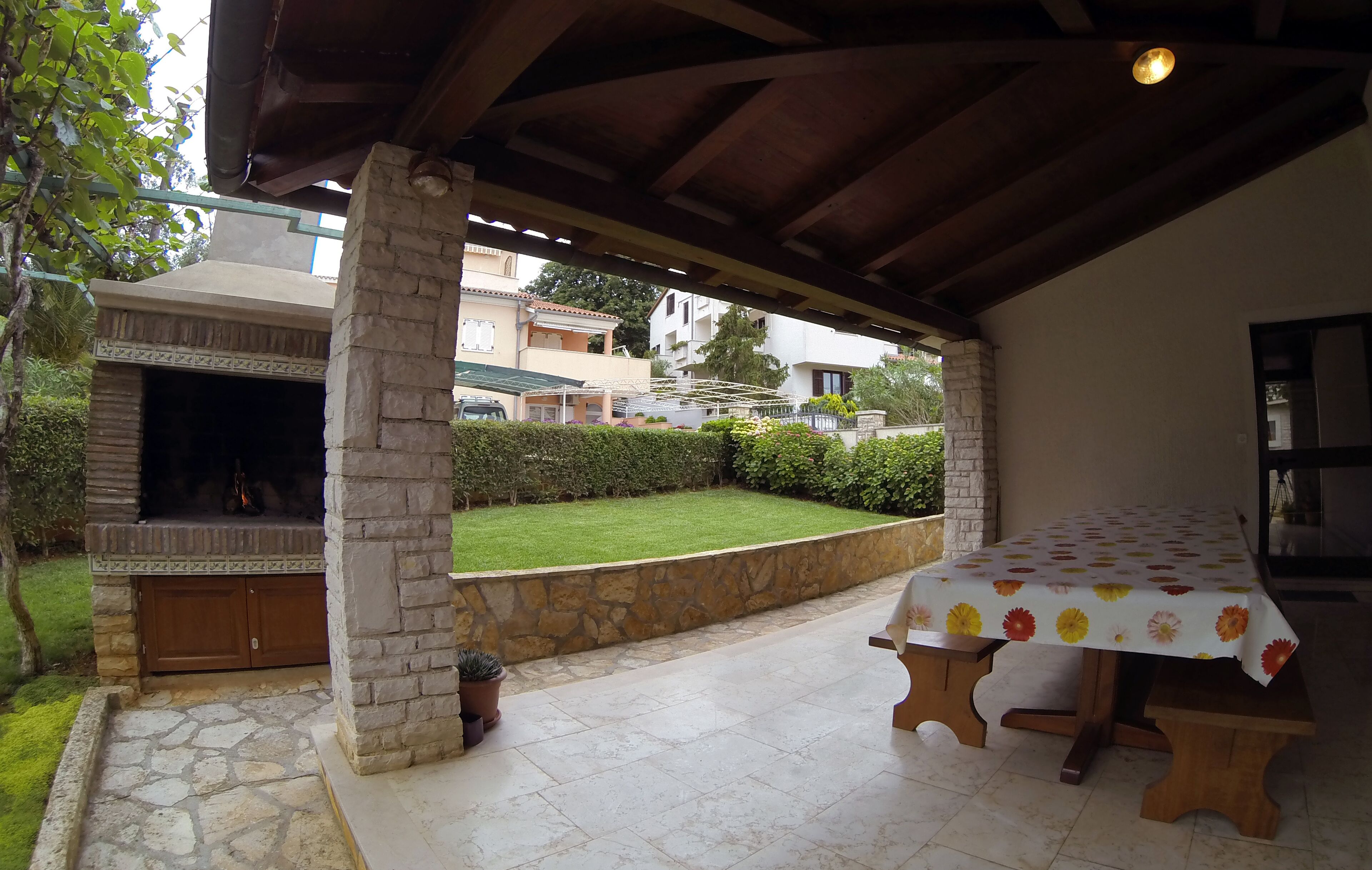 Un patio exterior con chimenea de piedra, un espacio de estar cubierto y vistas a casas vecinas.