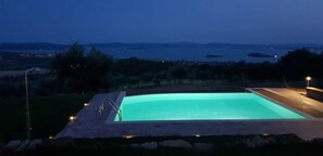 A swimming pool with a view of the sea and distant mountains at dusk.