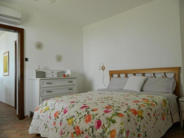 Quarto com colcha florida, cabeceira de madeira e mesa de cabeceira com abajur.
