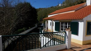 Un bâtiment blanc avec un toit recouvert de tuiles rouges, des volets verts et un portail en métal.