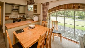 A compact kitchen with a wooden table and chairs, a view through a large window, and a door leading to a hallway.