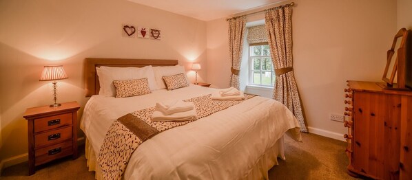 A neatly made bed with patterned pillows, a bedside lamp, and a wooden dresser.