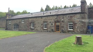 A stone building with a paved entrance, a wooden door, and a small garden area.