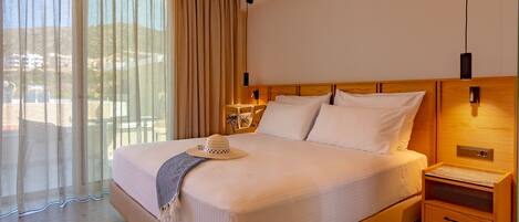 A hotel room with a large bed, a nightstand, a lamp, and a view of the outdoors through sheer curtains.