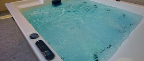 A hot tub with a control panel and a small seating area.