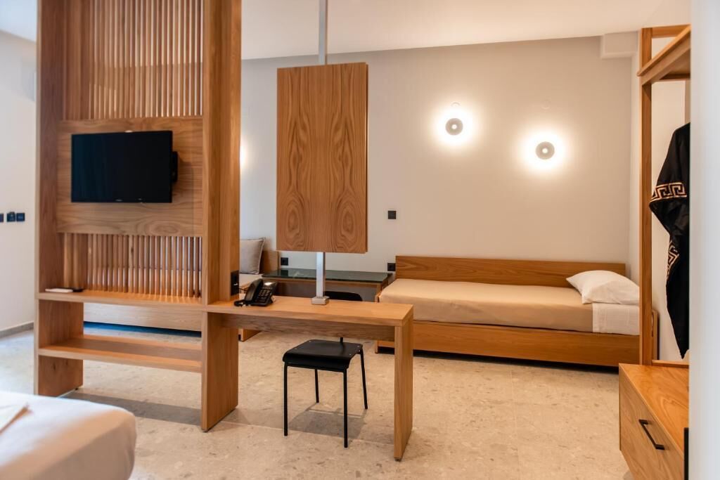 A modern bedroom with a wooden bed, a TV mounted on a wall, a desk with a chair, and a hanging light fixture.