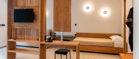 A modern bedroom with a wooden bed, a TV mounted on a wall, a desk with a chair, and a hanging light fixture.